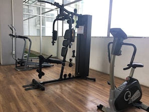 Uma academia com diversos equipamentos de exercícios, incluindo uma máquina multigym e uma elíptica.