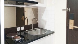 Cocina compacta con encimera negra, pileta de acero inoxidable y estufa con dos hornillas.