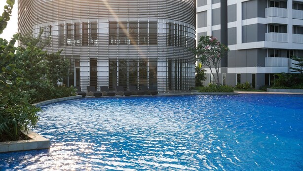 Ein modernes Gebäude mit gewölbter Fassade, einem Swimmingpool und umgebender Bepflanzung.