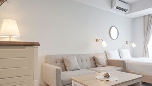 Ein modernes Hotelzimmer mit einer Couch, einem Bett, einem kleinen Tisch mit einem dekorativen Gegenstand und einer Wand-Klimaanlage.