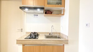 A compact kitchen with a gas stove, a sink, and wooden cabinets. - Fully Furnished And Homey 3Br At Meikarta Apartment (Cikarang)
