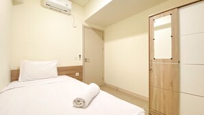 A hotel room with a bed, a wooden wardrobe, and a wall-mounted air conditioning unit. - Fully Furnished And Homey 3Br At Meikarta Apartment (Cikarang)