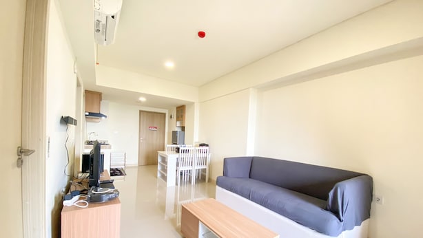 A modern living room with a grey sofa, a wooden coffee table, and a TV stand. - Fully Furnished And Homey 3Br At Meikarta Apartment (Cikarang)