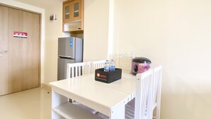 A compact kitchen with a refrigerator, a microwave, and a toaster. There is a white table with a tray of bottled water and a box of travel essentials. - Fully Furnished And Homey 3Br At Meikarta Apartment (Cikarang)
