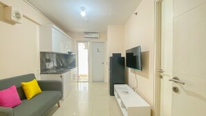 A modern living room with a grey sofa, a white side table, and a flat-screen TV mounted on the wall. - Minimalist And Good Deal 2Br At Bassura City Apartment (Jakarta)