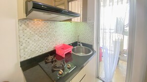 A kitchen with a gas stove, a stainless steel sink, and a red dish rack. - Good Deal And Minimalist 2Br At Bassura City Apartment (Jakarta)