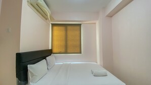 A neatly made bed with white linens, a black headboard, and a window with blinds. - Good Deal And Minimalist 2Br At Bassura City Apartment (Jakarta)