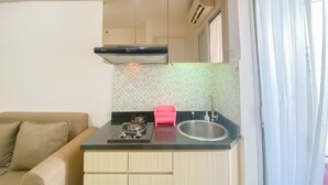 A compact kitchen with a gas stove, a sink, and a small countertop. There is a beige sofa in the adjacent living area. - Good Deal And Minimalist 2Br At Bassura City Apartment (Jakarta)
