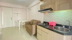 A modern kitchen with a black countertop, stainless steel sink, and a beige sofa. - Good Deal And Minimalist 2Br At Bassura City Apartment (Jakarta)