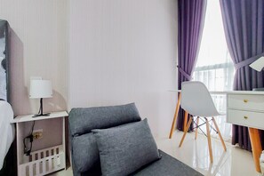 Une chambre d’hôtel avec un lit, un bureau doté d’une lampe, une chaise grise et une commode blanche.