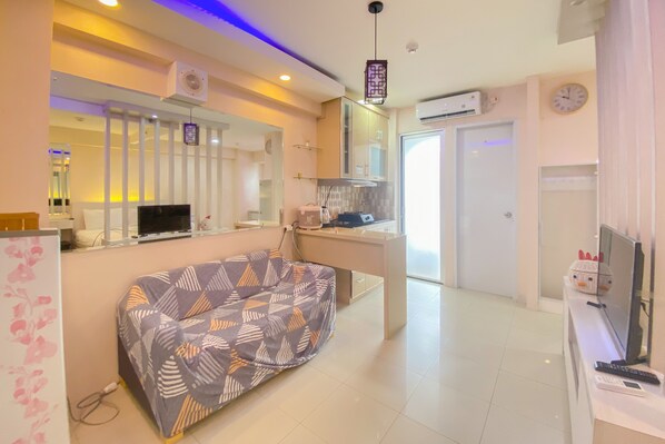 A modern hotel room with a sofa, a desk with a computer, a TV, and a clock on the wall. - Best Deal And Spacious Studio At Bassura City Apartment (Jakarta)