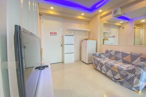 A hotel room with a bed, a desk, a chair, a wardrobe, a refrigerator, and a mirror.