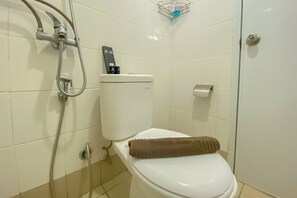 A bathroom with a toilet, a shower, and a toilet paper holder. - Best Deal And Spacious Studio At Bassura City Apartment (Jakarta)