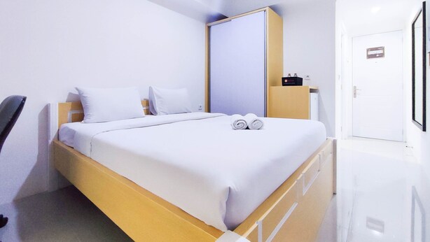 A modern hotel room with a single bed, a wooden headboard, a bedside table with a lamp, and a large mirror on the wall. - Cozy Studio At 9Th Floor Paltrow City Apartment (Semarang)