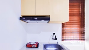 A compact kitchen with a built-in stove, a sink, and a window with blinds. - Cozy Studio At 9Th Floor Paltrow City Apartment (Semarang)