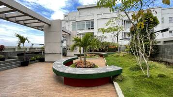 Un edificio moderno con un espacio exterior techado que presenta un macetero curvo con vegetación, un sendero empedrado y vistas del exterior del edificio.