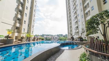 Una piscina rodeada de edificios residenciales altos con balcones, cielo despejado y algo de vegetación.