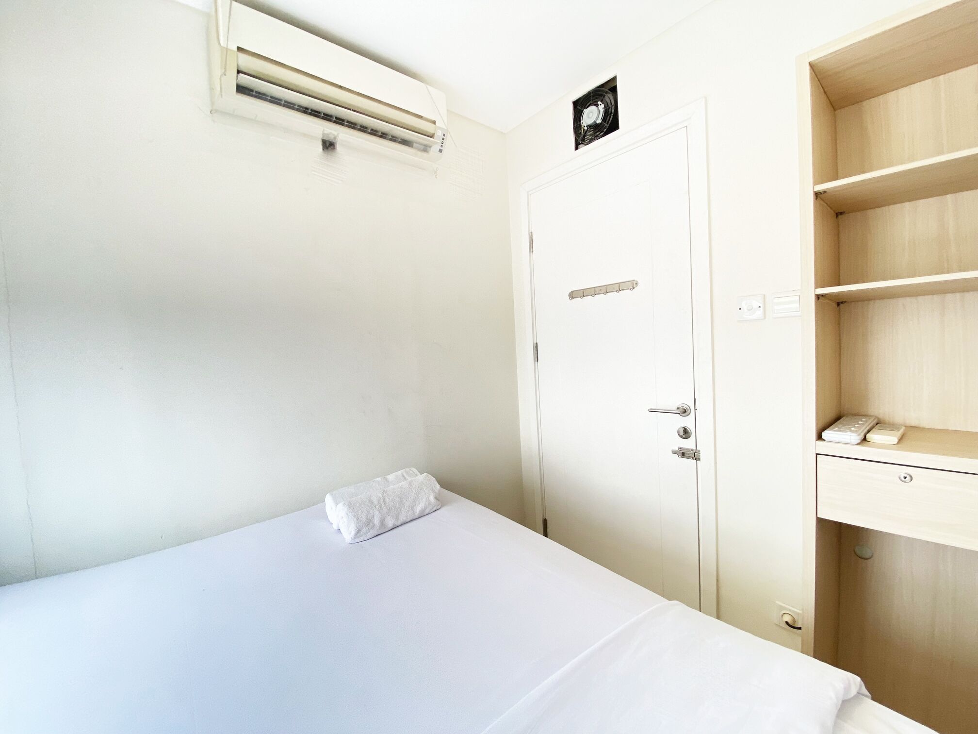 Une chambre d’hôtel avec un lit, une armoire et une étagère sur laquelle se trouve un téléphone.