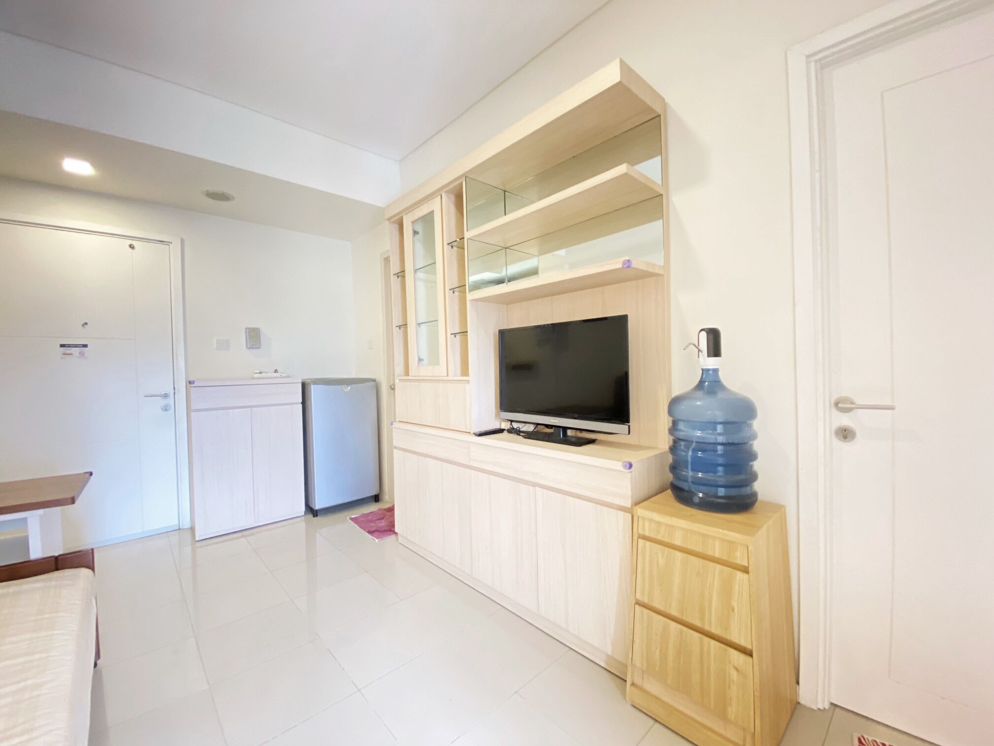 Un espacio habitable compacto con kitchenette, televisor y un dispensador de agua grande.