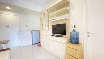 Un espacio habitable compacto con kitchenette, televisor y un dispensador de agua grande.
