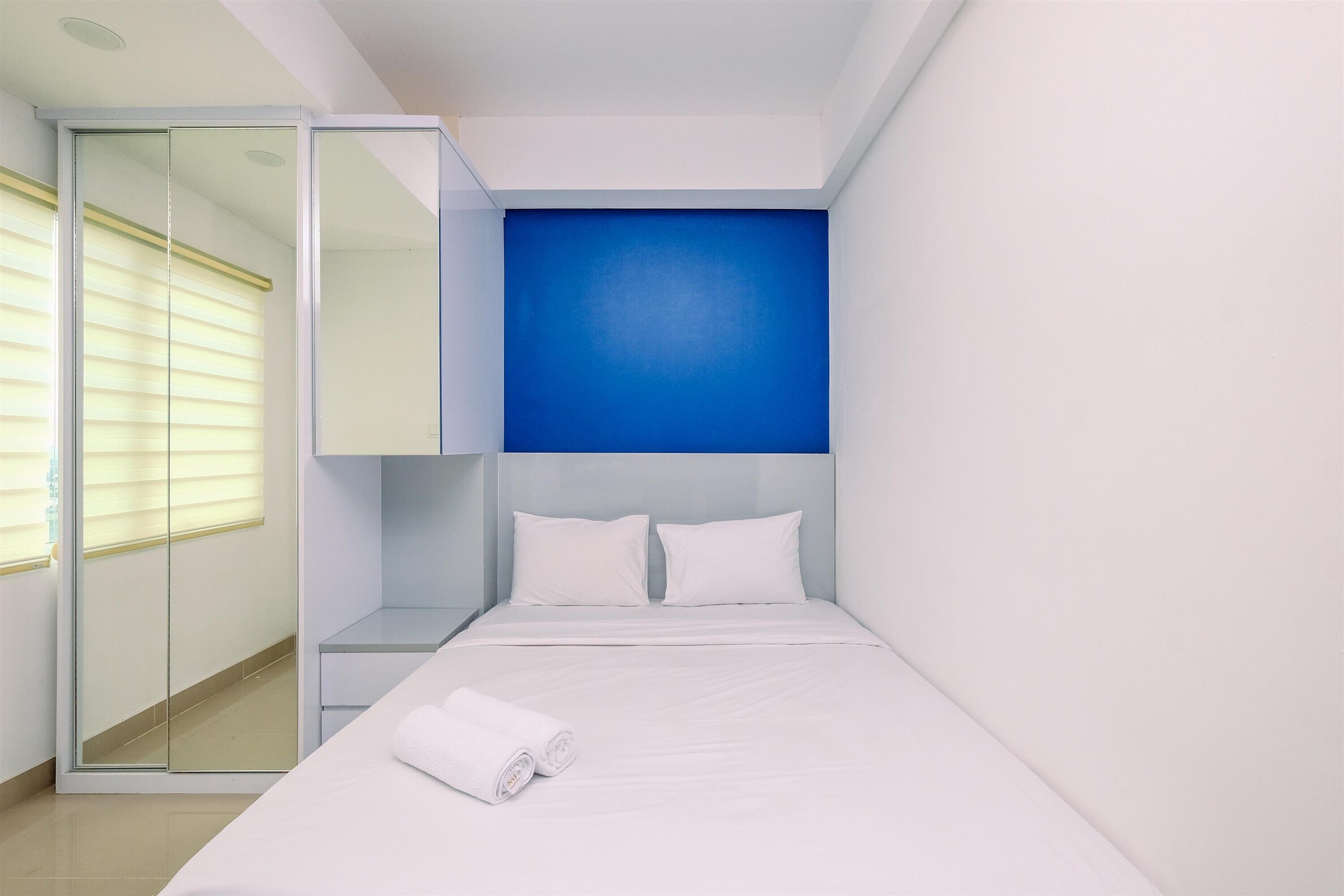 A modern hotel room with a large bed, a glass wardrobe, and a blue accent wall.