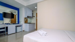 A hotel room with a bed, a desk, a chair, a TV, a kitchenette, and a bathroom. - Elegant Studio Apartment At B Residence Near Aeon Mall (Pagedangan)