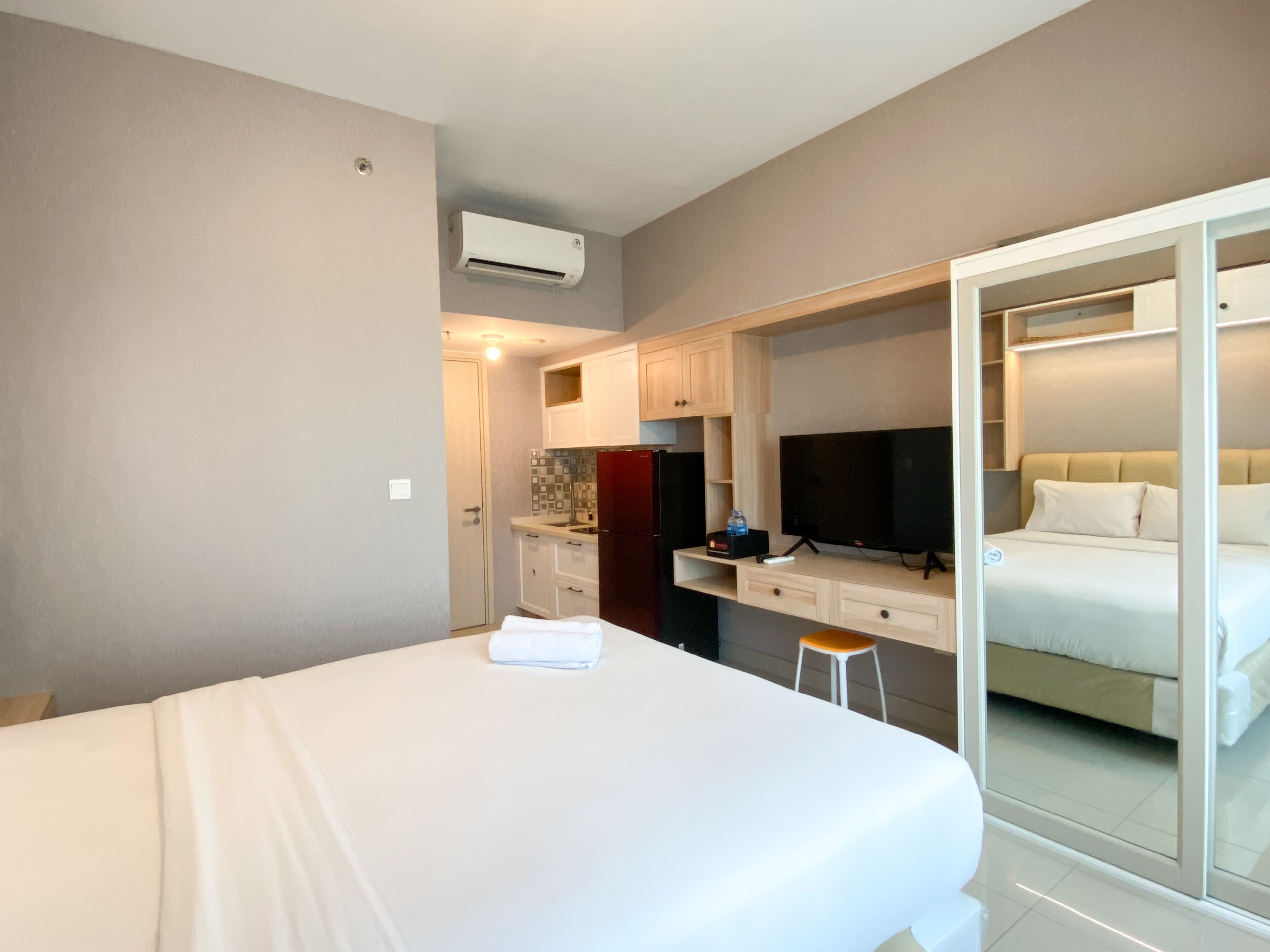 A hotel room with a bed, a TV, a small kitchen area, and a sliding door leading to another room.