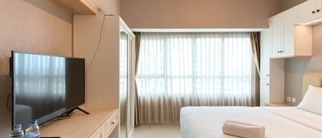 Habitación de hotel con cama, televisor, escritorio y silla, y ventana con cortinas.