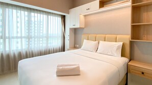Ein modernes Hotelzimmer mit einem großen Bett, einem Nachttisch, einer integrierten Ablage und einem Fenster mit durchsichtigen Vorhängen.