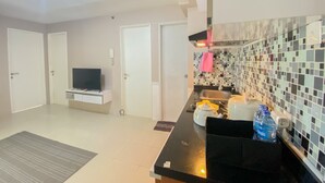 A modern kitchen with a black countertop, a tiled backsplash, and a television on a white cabinet. - Nice Comfortable 2Br Apartment At Bassura City (Jakarta)
