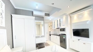 A modern kitchen with white cabinets, a built-in microwave, and a large flat-screen TV. - Nice Studio Room At Grand Asia Afrika Apartment (Bandung)