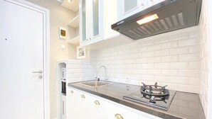 A compact kitchen with white cabinets, a stainless steel sink, and a gas stove. - Nice Studio Room At Grand Asia Afrika Apartment (Bandung)