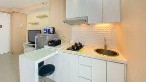 Una cocina compacta con gabinetes blancos, estufa a gas, lavamanos y un pequeño espacio tipo barra con taburetes.