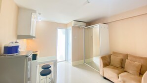 Una sala de estar moderna con un sofá color beige, un box de ducha de vidrio, una kitchenette con tostadora y un taburete pequeño.