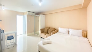 Habitación de hotel con cama, zona de estar con sofá y sillas, una mesita y un vidrio que da al baño.