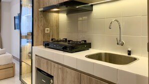 A modern kitchen with a built-in stove, stainless steel sink, and wooden cabinetry. - Cozy Studio At Tokyo Riverside Pik 2 Apartment (Teluknaga)