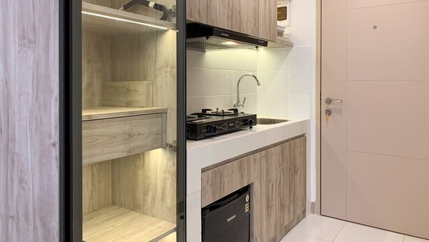 A modern kitchen with wooden cabinets, a built-in stove, and a dishwasher. - Cozy Studio At Tokyo Riverside Pik 2 Apartment (Teluknaga)