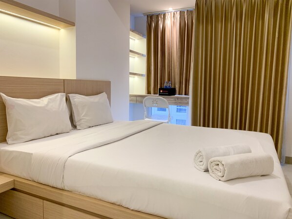 A neatly made bed with white linens and pillows, a wooden headboard, and a small bedside table with a bottle of water and a black box.