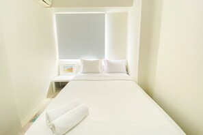 A narrow hotel room with a single bed, a window with blinds, and a small bedside table with a lamp. - Beautiful And Cozy 2Br Bassura City Apartment (Jakarta)