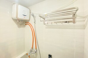 A bathroom with a wall-mounted shower unit, a towel rack, and a visible electrical outlet. - Beautiful And Cozy 2Br Bassura City Apartment (Jakarta)