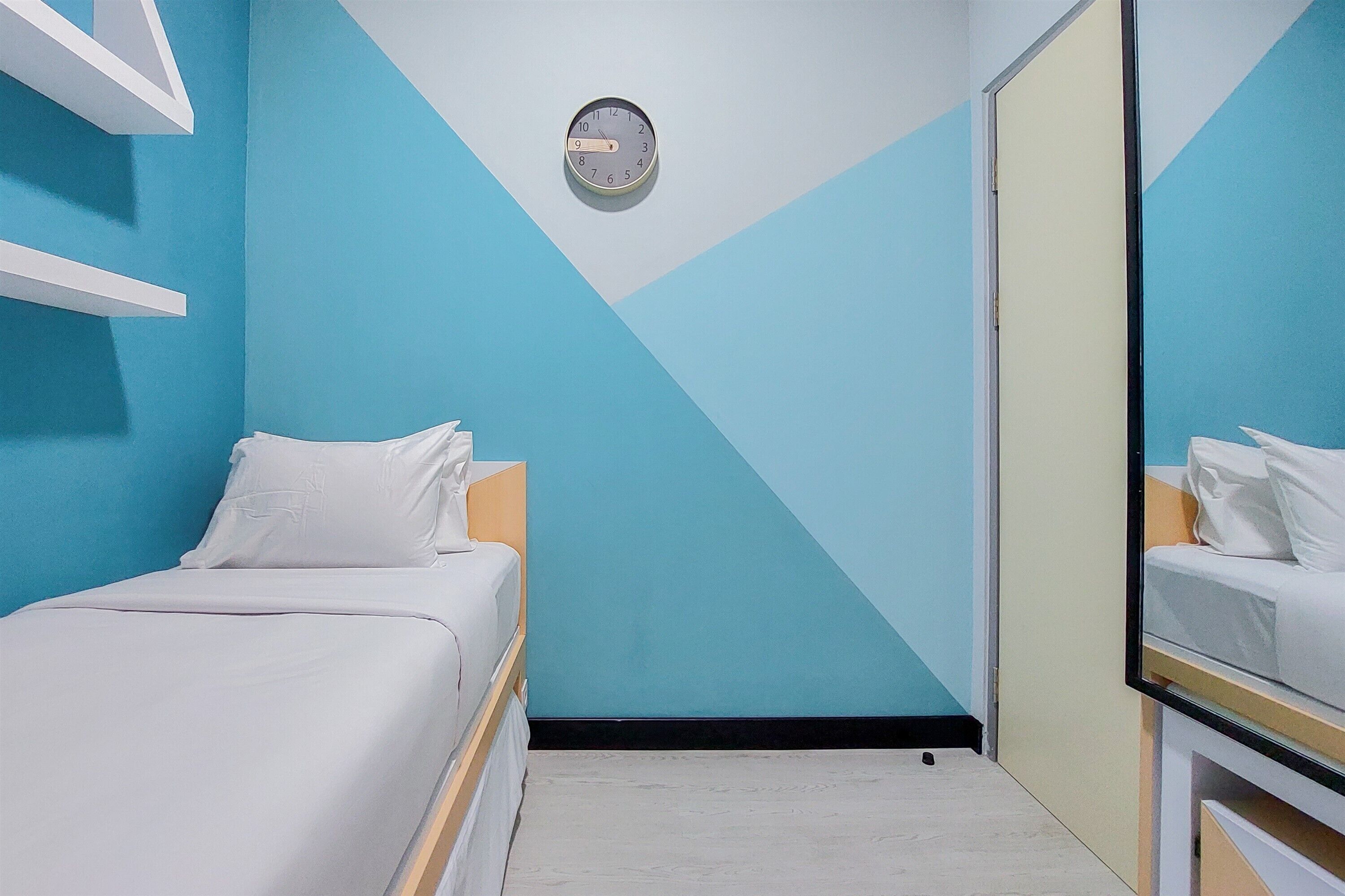 A room with a bed, a clock on the wall, and a mirror reflecting the bed.