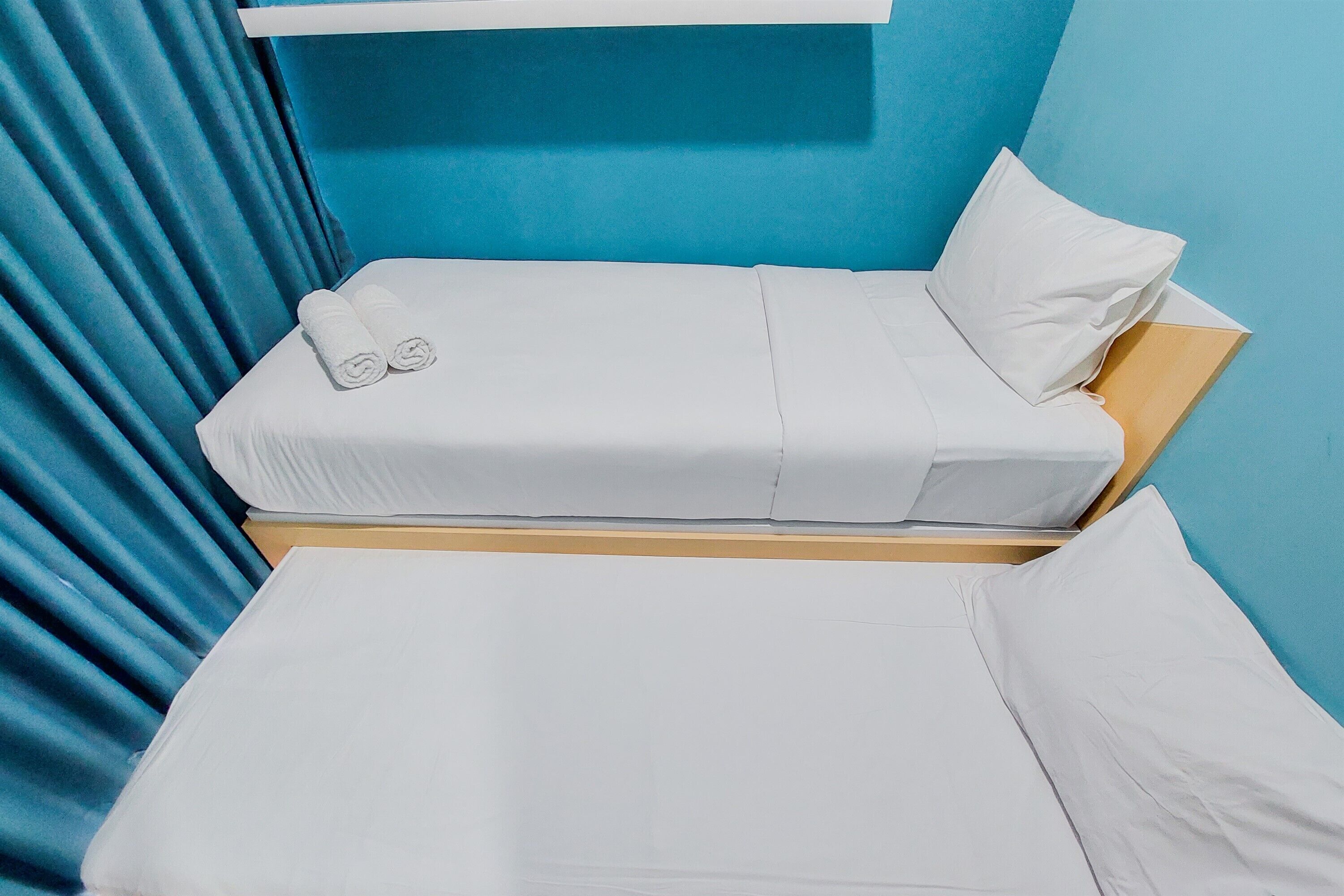 Cama doble con sábanas blancas y dos toallas enrolladas, frente a una pared azul con cabecera de madera.