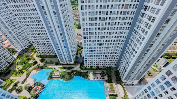 A high-rise residential building complex with a central swimming pool surrounded by greenery and pathways. - Scenic And Comfortable 2Br Apartment M-Town Residence (Gading Serpong)