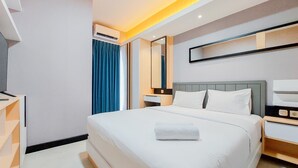 A modern hotel room with a large bed, a bedside table, a TV, and a mirror. - Scenic And Comfortable 2Br Apartment M-Town Residence (Gading Serpong)