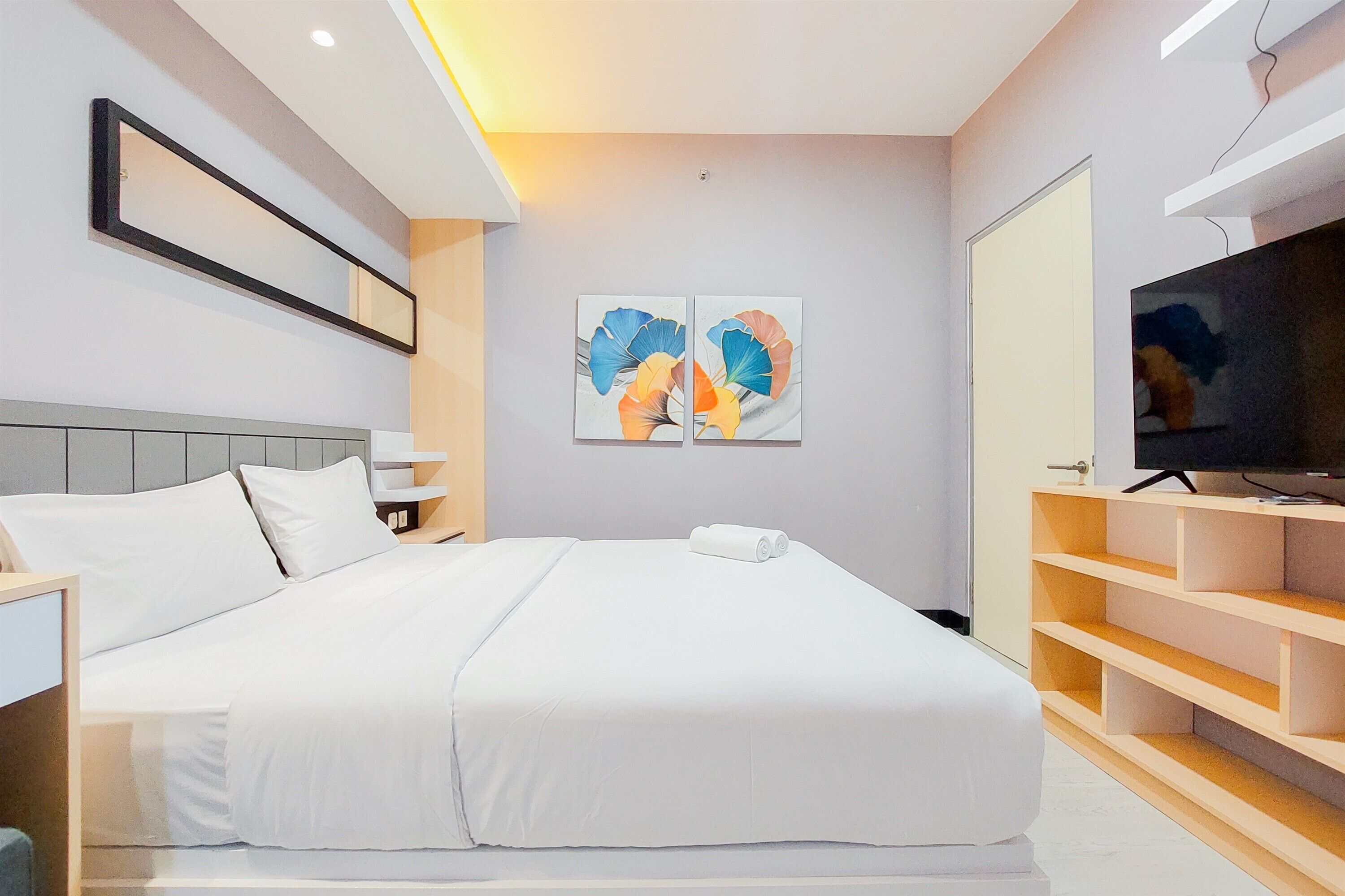 A modern hotel room with a large bed, a TV, and artwork on the wall.