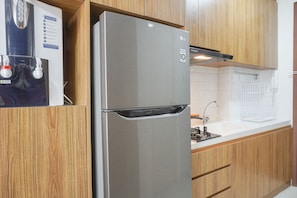 A stainless steel refrigerator with a water dispenser, wooden cabinets, and a white countertop with a sink.