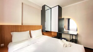 A hotel room with a large bed, a wooden headboard, a bedside table with a lamp, and a mirror. - Nice 2Br At Gateway Pasteur Apartment (Cimahi)