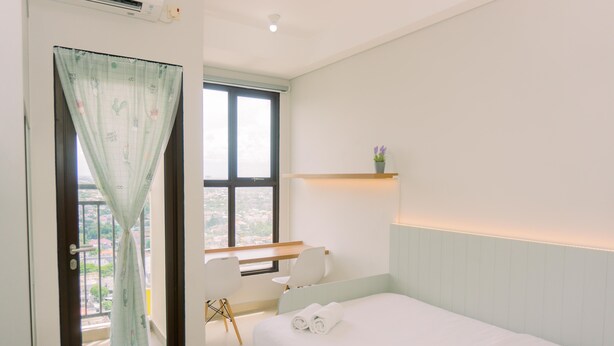 A bedroom with a bed, a desk, a chair, a window with a curtain, and a small shelf with a plant. - Good Deal And Simply Look Studio Room At Transpark Bintaro Apartment (South Tangerang)