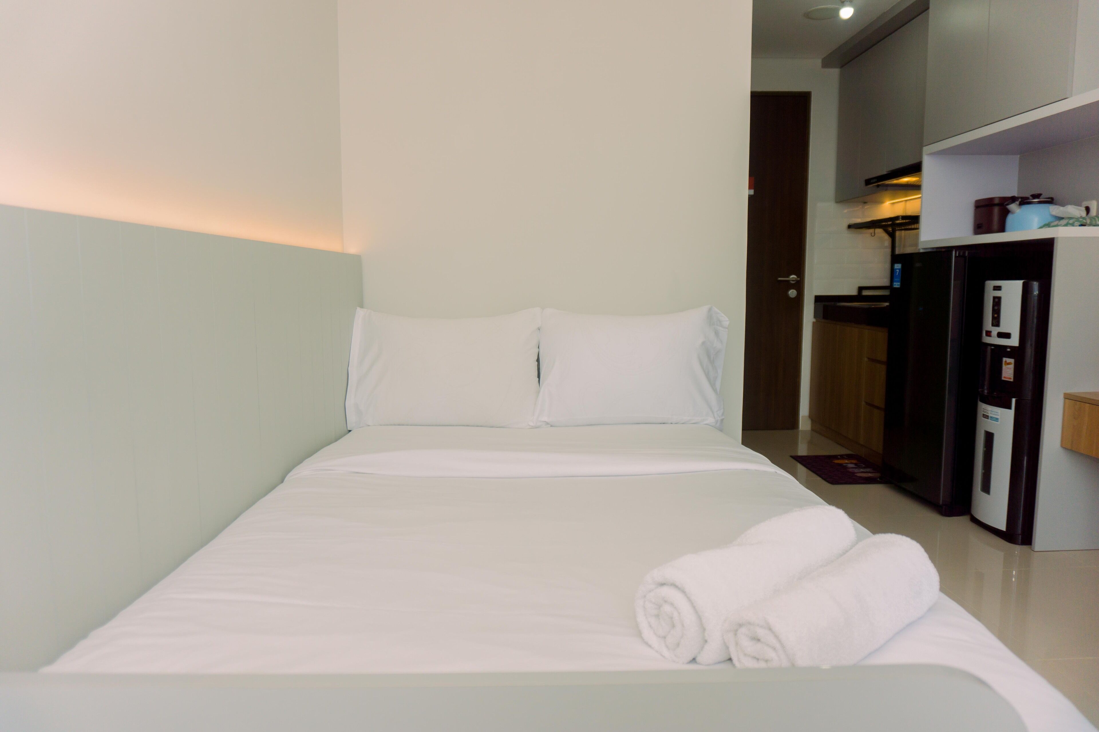 A hotel room with a bed, a small kitchenette, and a door leading to another room.