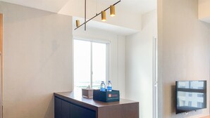 A modern hotel room with a wooden desk, a flat-screen TV, and a window with a view. - Stylisth 1Br At Tokyo Riverside Pik 2 Apartment (Teluknaga)